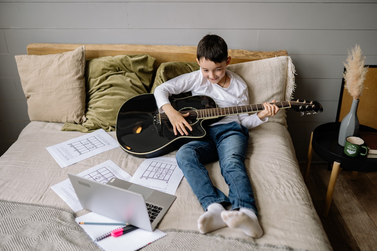 Boy Sitting on Bed While Learning to Play Guitar | Kids Car Donations