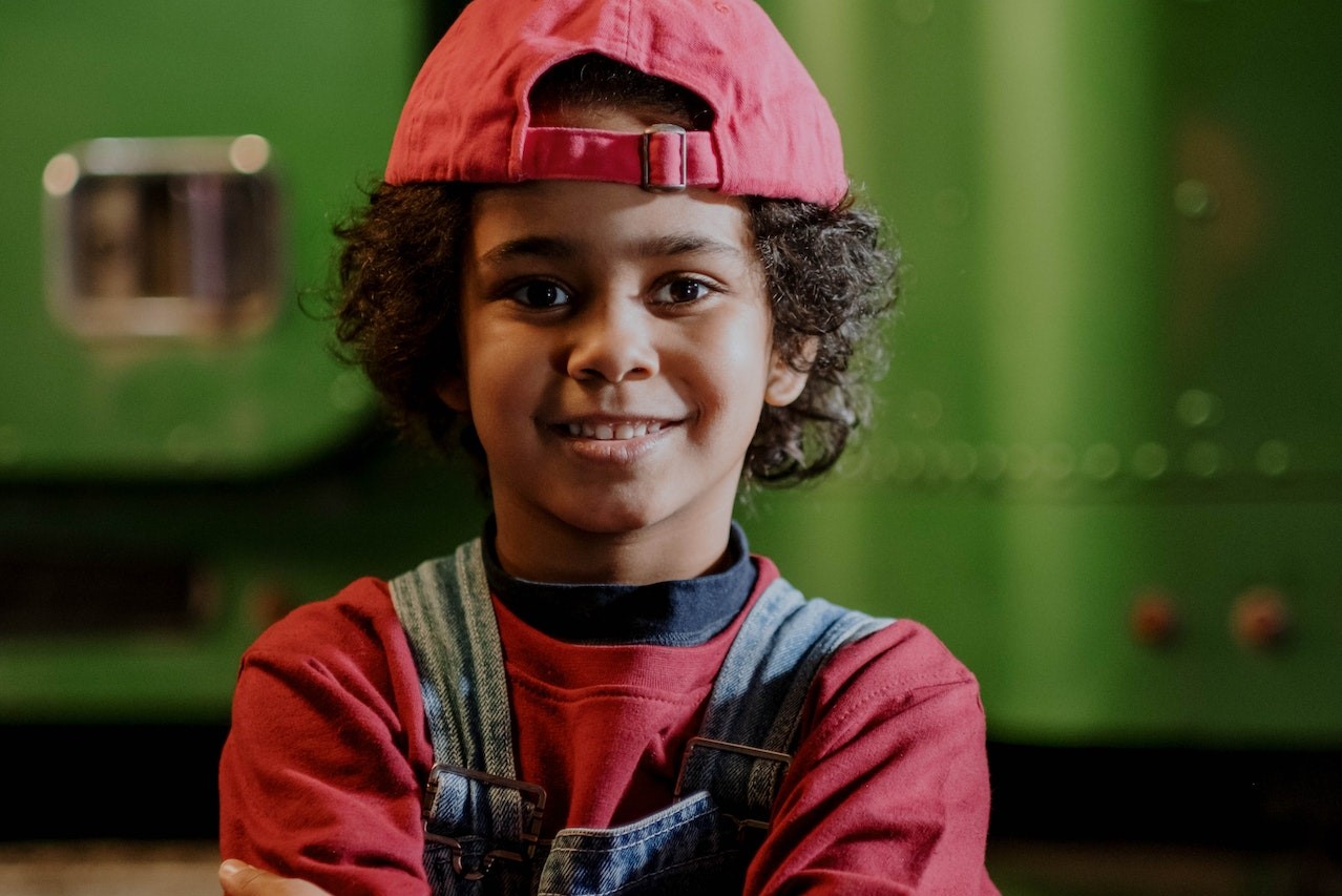 Standing Boy Wearing a Red Cap and Denim Overall | Kids Car Donations