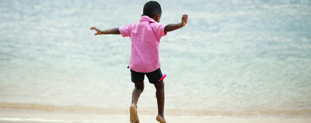 Kid wearing pink shirt playing at the beach | Kids Car Donations