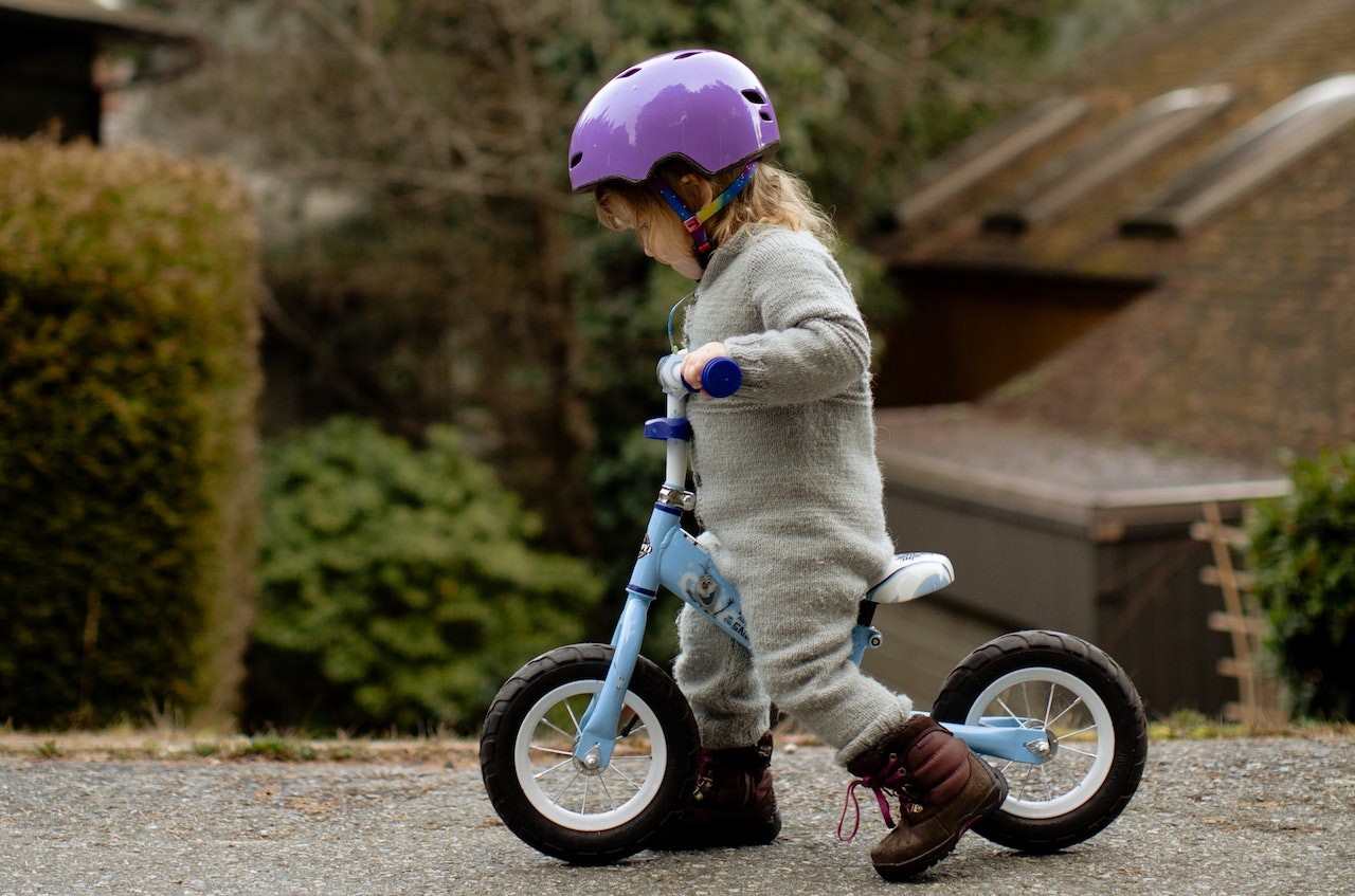 Little girl in helmet riding run bike on street | Kids Car Donations
