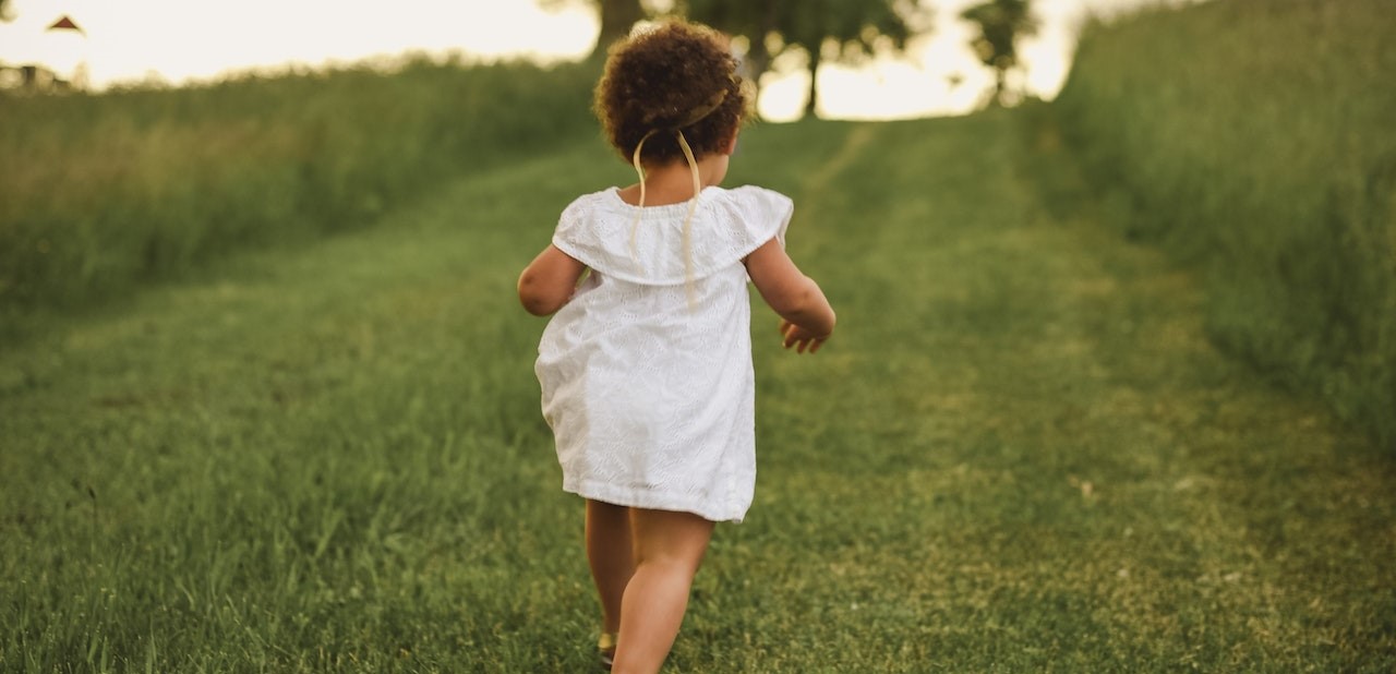 Girl Standing on Grass Field Facing Trees | Kids Car Donations