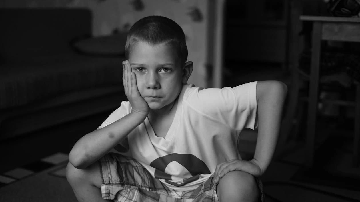 Black and white photo of a boy sitting on the floor looking thoughtful