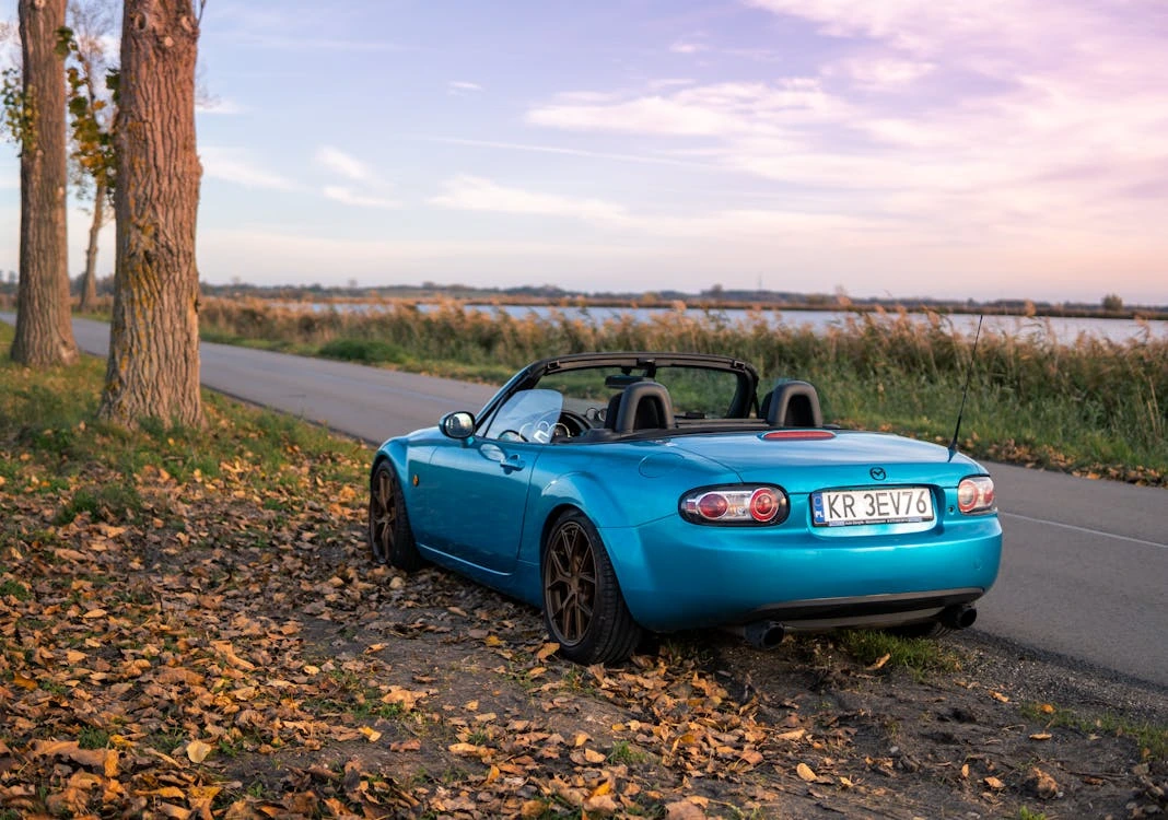 Blue Mazda MX-5 convertible parked by a scenic road in autumn