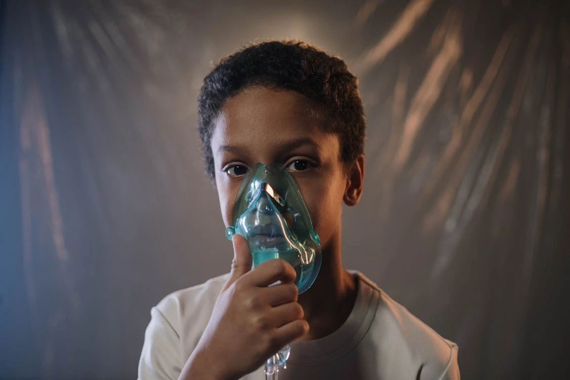 Boy in a white shirt holding a green oxygen mask