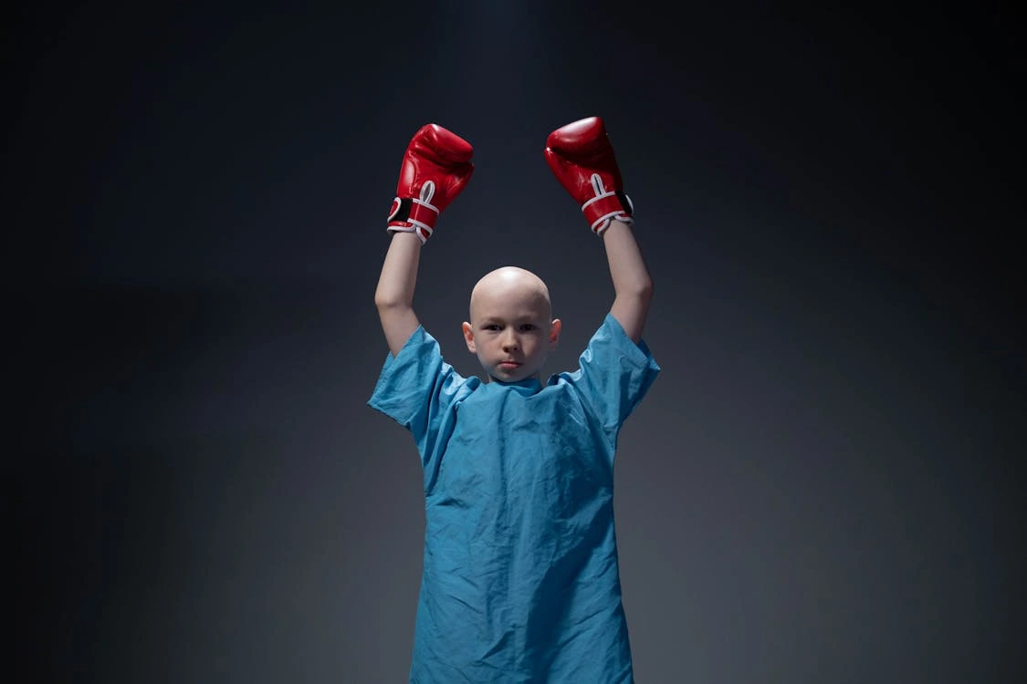A boy with cancer wearing gloves while posing at the camera