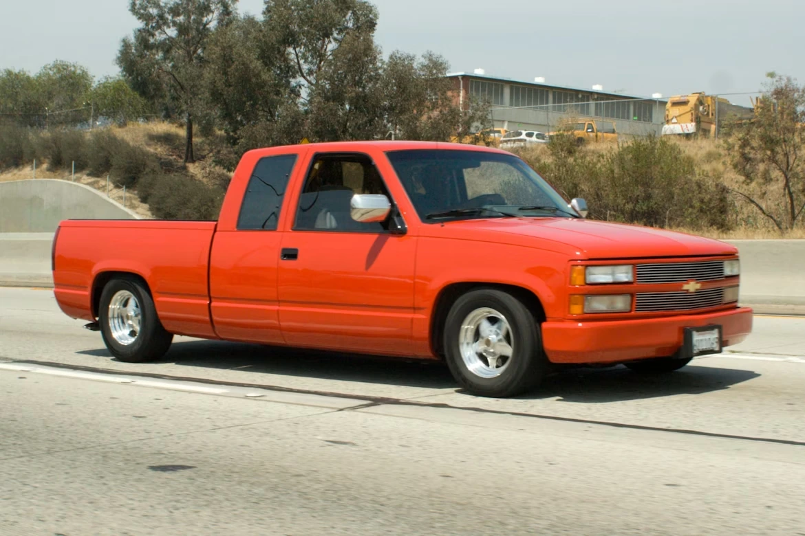 Red Chevrolet single cab pickup truck parked beside a green tree during daytime