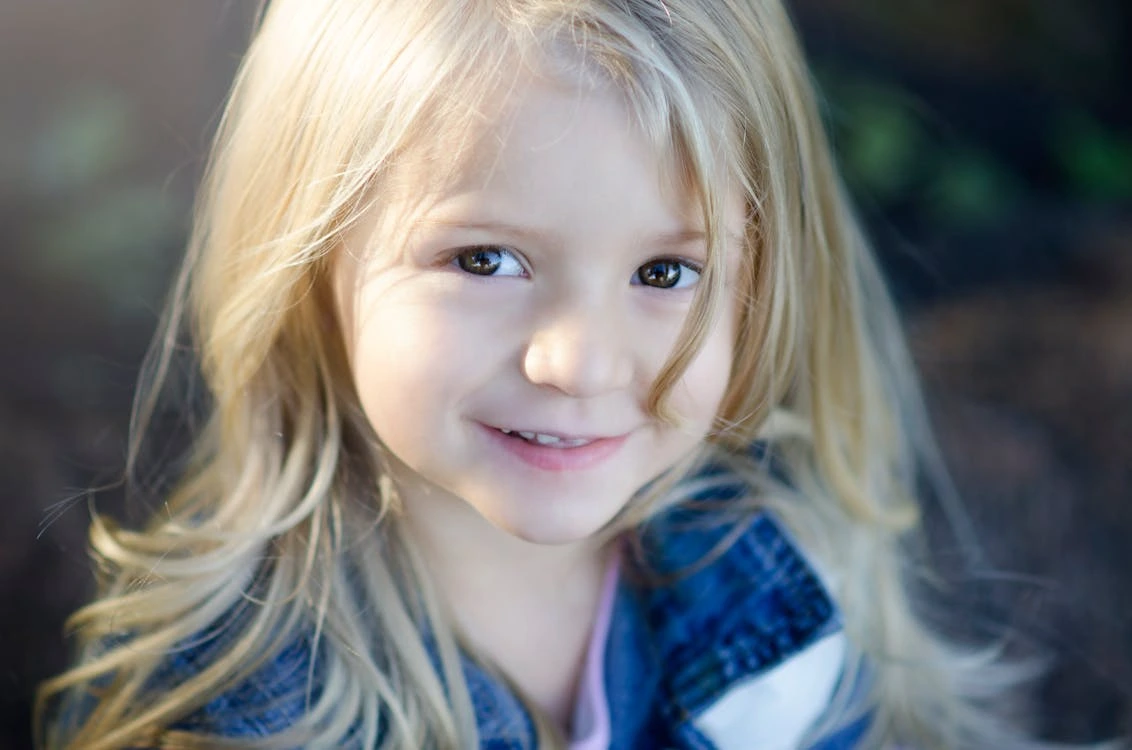 A close-up shot of a girl with blonde hair smiling outdoors
