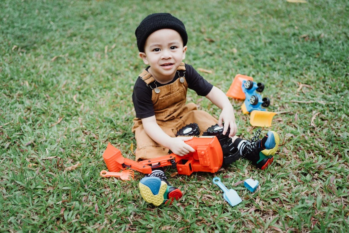 A young boy sitting on the grass while playing with toys