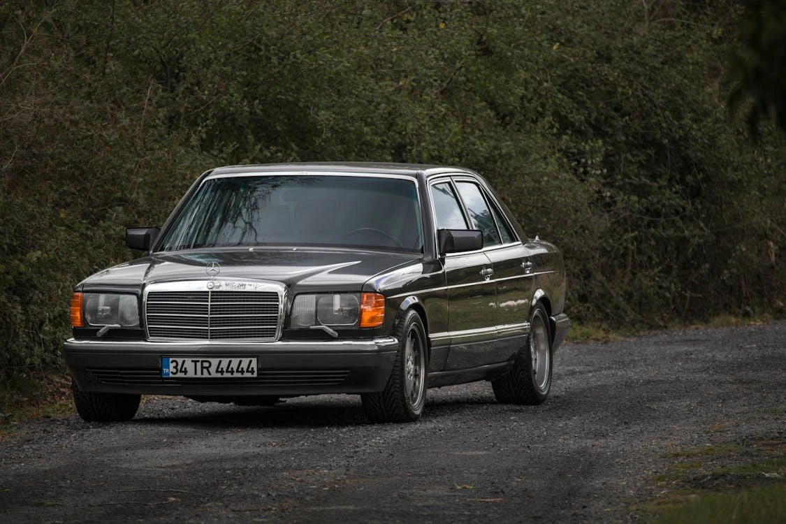 Black Mercedes-Benz parked on a dirt road in a forest setting