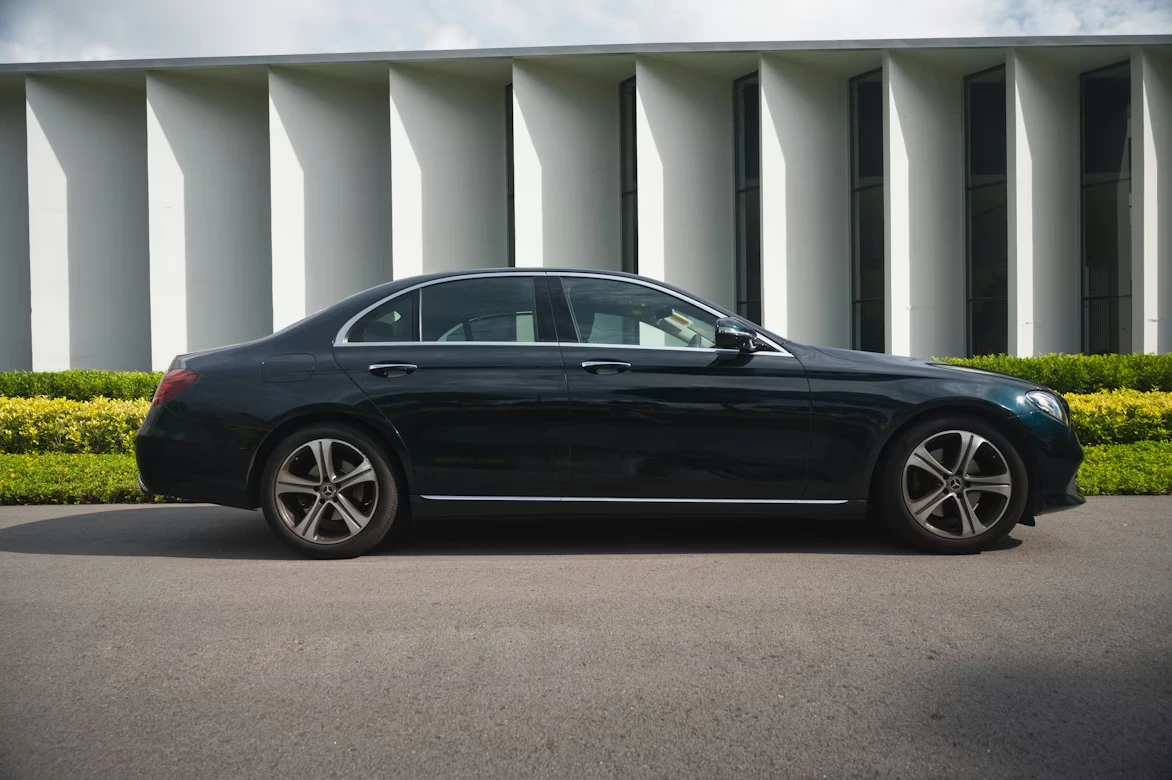 Black sedan parked near a white building on a sunny street
