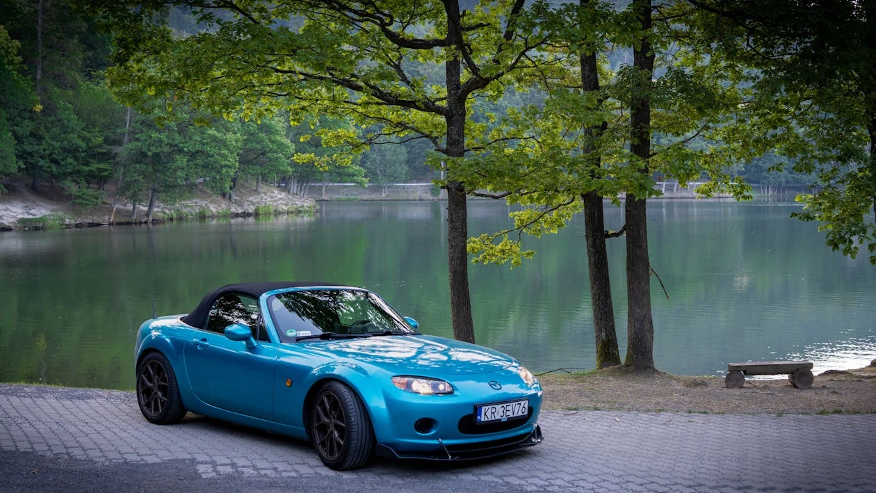 Blue Mazda MX-5 convertible parked by a serene lakeshore