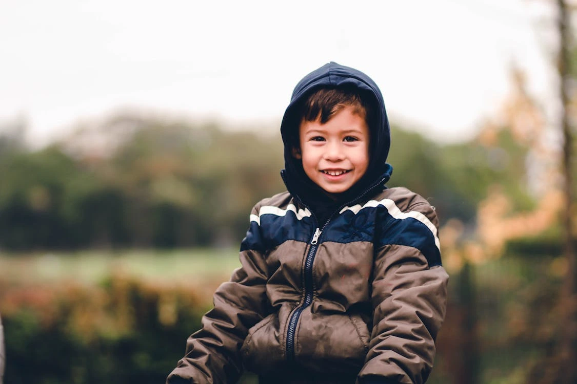 Boy smiling and wearing a hooded jacket outdoors