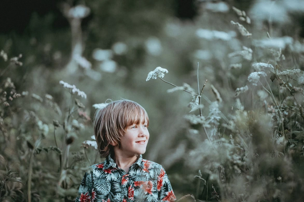 Boy in a red and green floral button-up collared top smiling in tall grasses