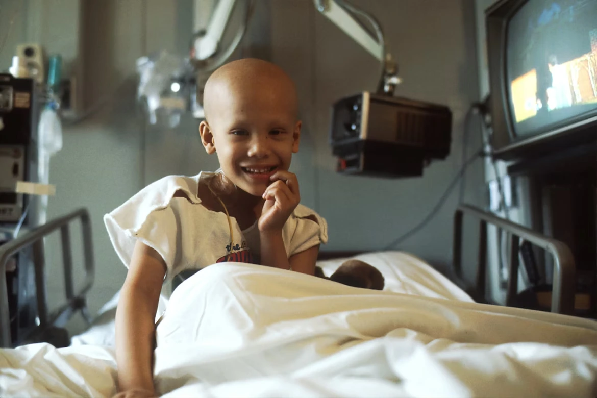 Child with cancer sitting on a bed