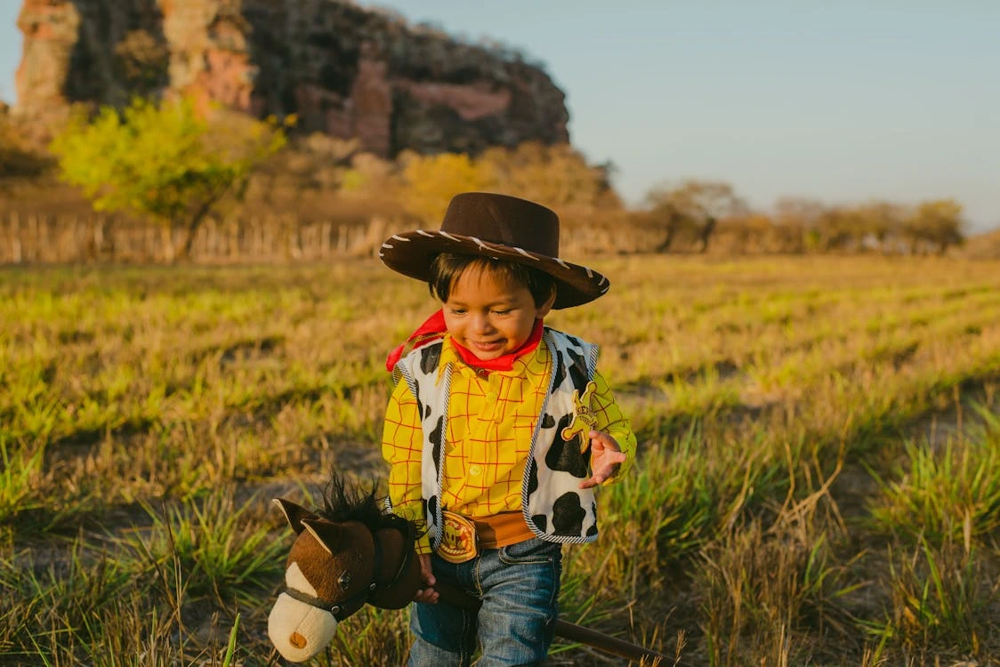 Child wearing a cowboy costume walking across a grassy field
