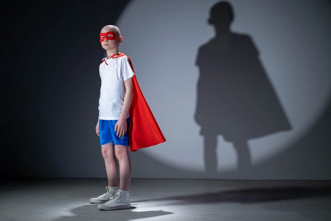 Child wearing a mask and cape striking a superhero pose