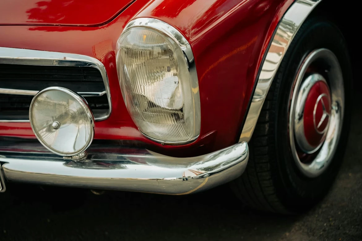 Close-up of a vintage red car’s headlight and fender
