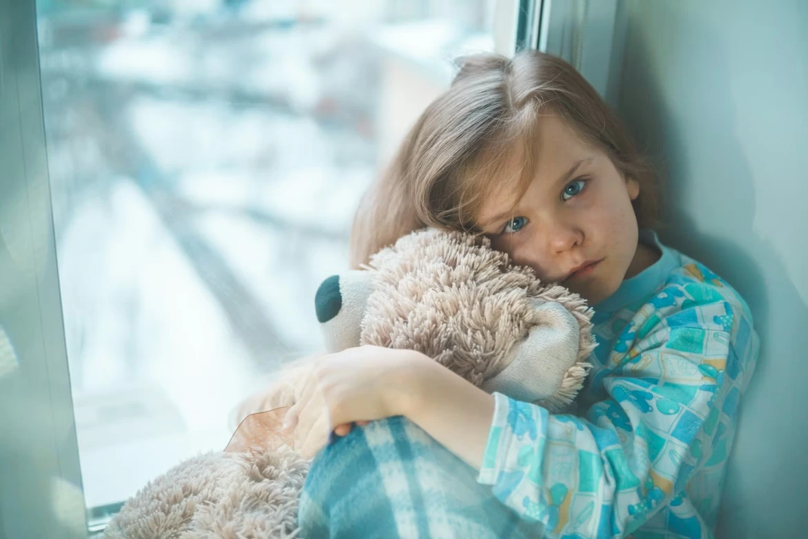 Girl in blue, white, and red plaid shirt hugging brown teddy bear