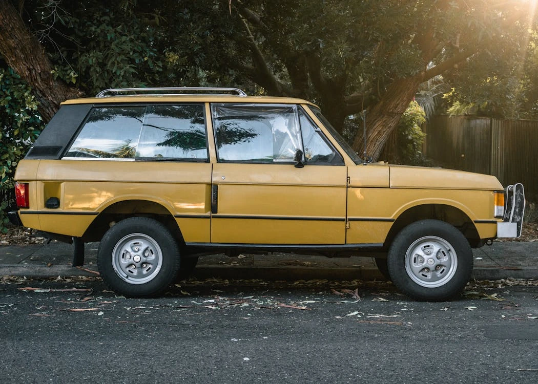 Side view of a classic yellow SUV parked on a tree-lined urban street