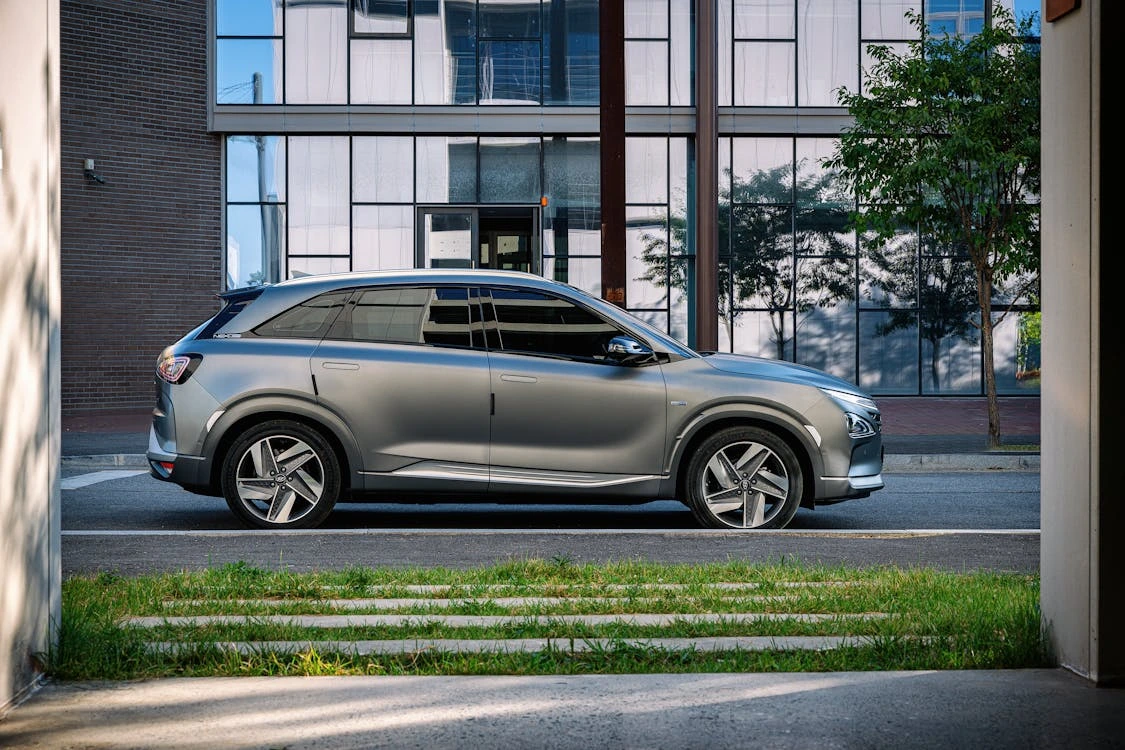 Side view shot of gray SUV parked near a glass building