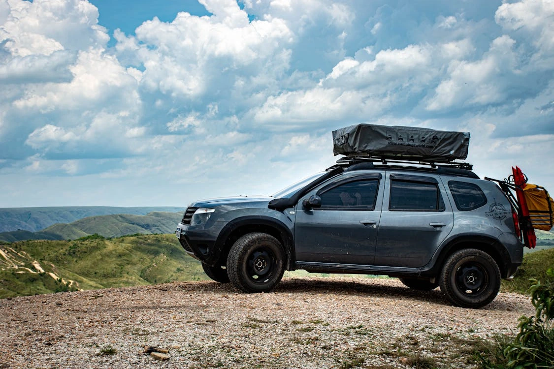 SUV with a roof tent on a hill overlooking a scenic landscape