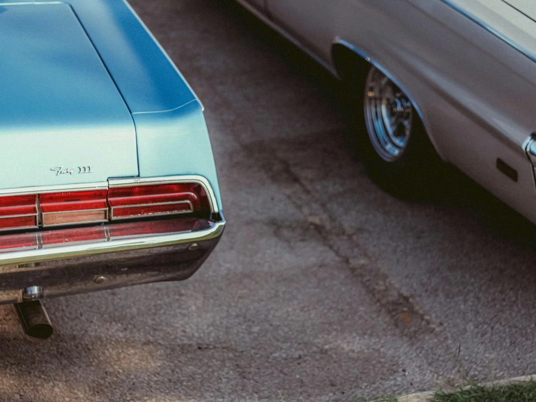 Two classic cars parked on a driveway in front of a mid-century home