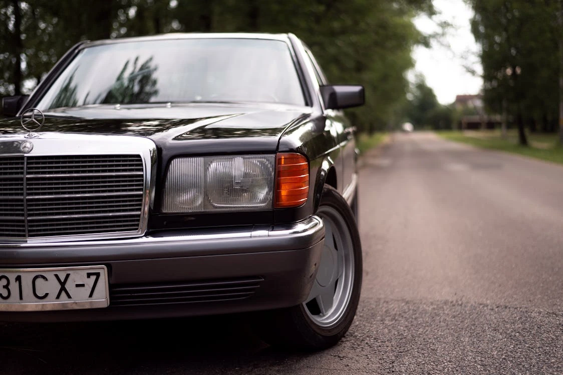 Vintage black Mercedes-Benz W126 on a road surrounded